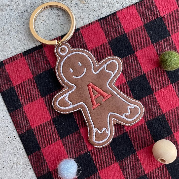 In-the-hoop machine embroidery design of a gingerbread cookie keychain made of leather, featuring a personalized letter "A" initial, with applique stitching.